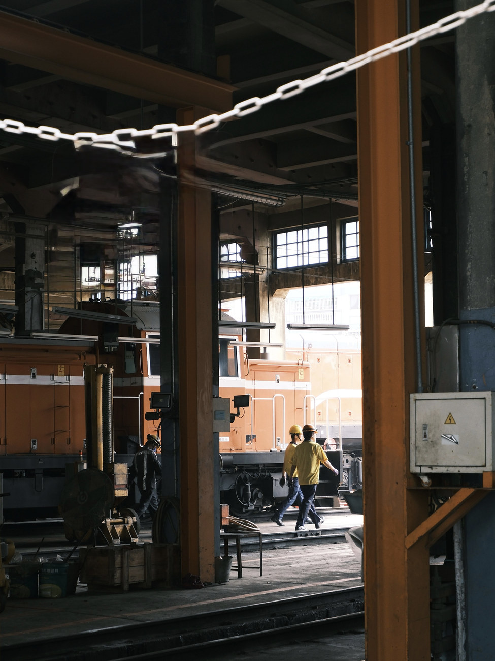 Shop crew crossing the floor of a locomotive shed between orange diesel units
